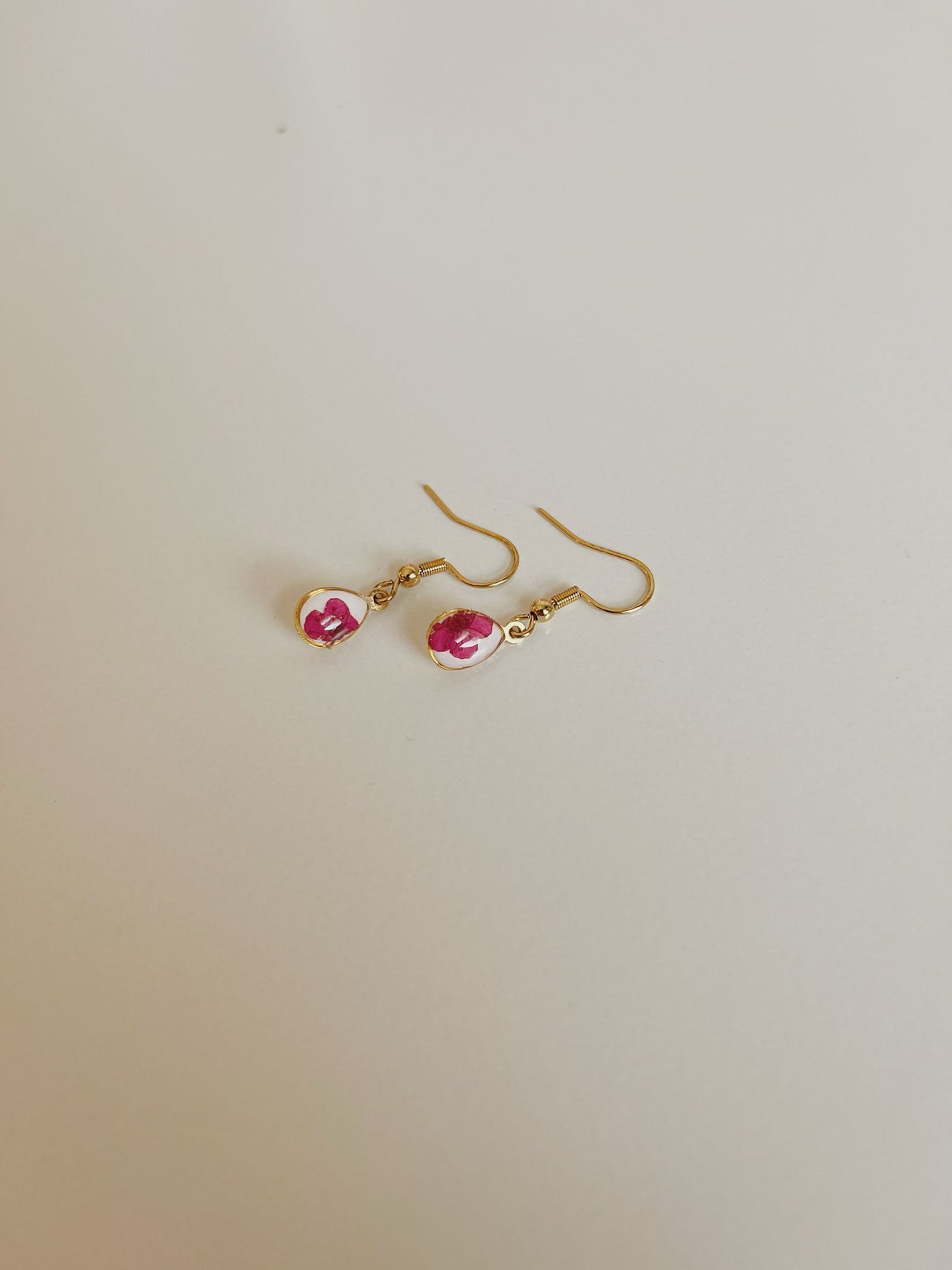 Gold earrings with pink gemstones on a light gray background