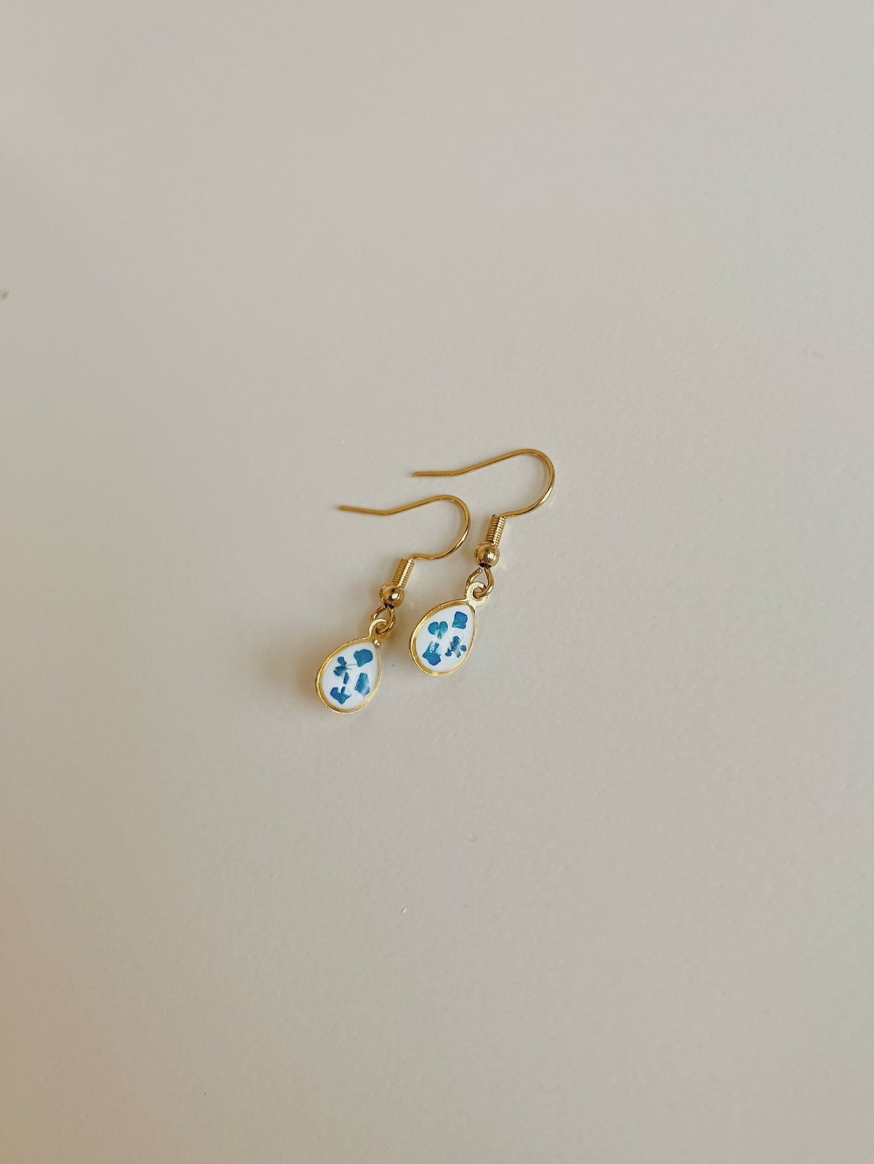Gold earrings with blue and white floral designs on a light gray background