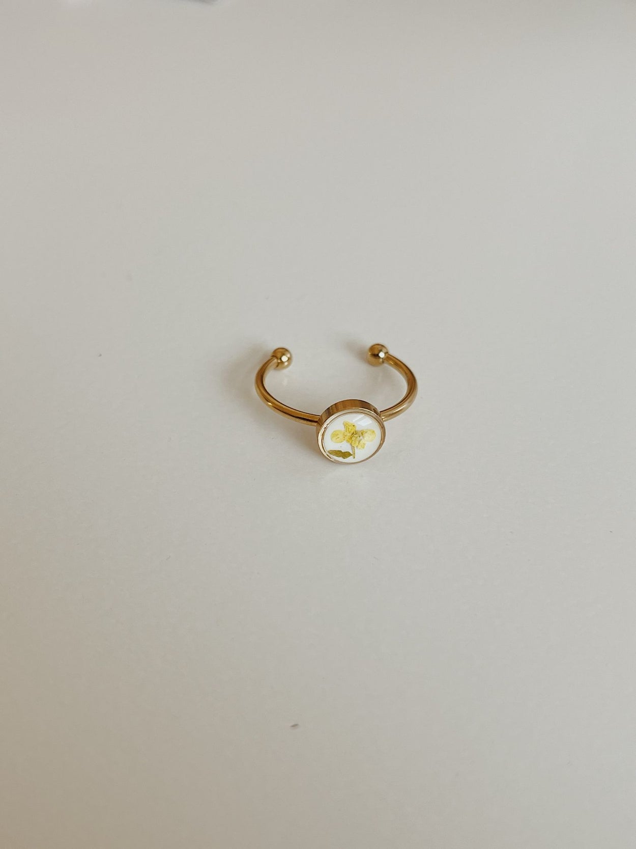 Gold ring with a round white stone on a light gray background
