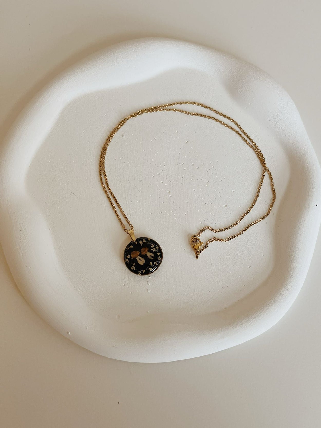 Necklace with a round pendant on a white ceramic dish