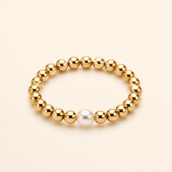 A gold-colored bracelet with a single white pearl bead in the center.