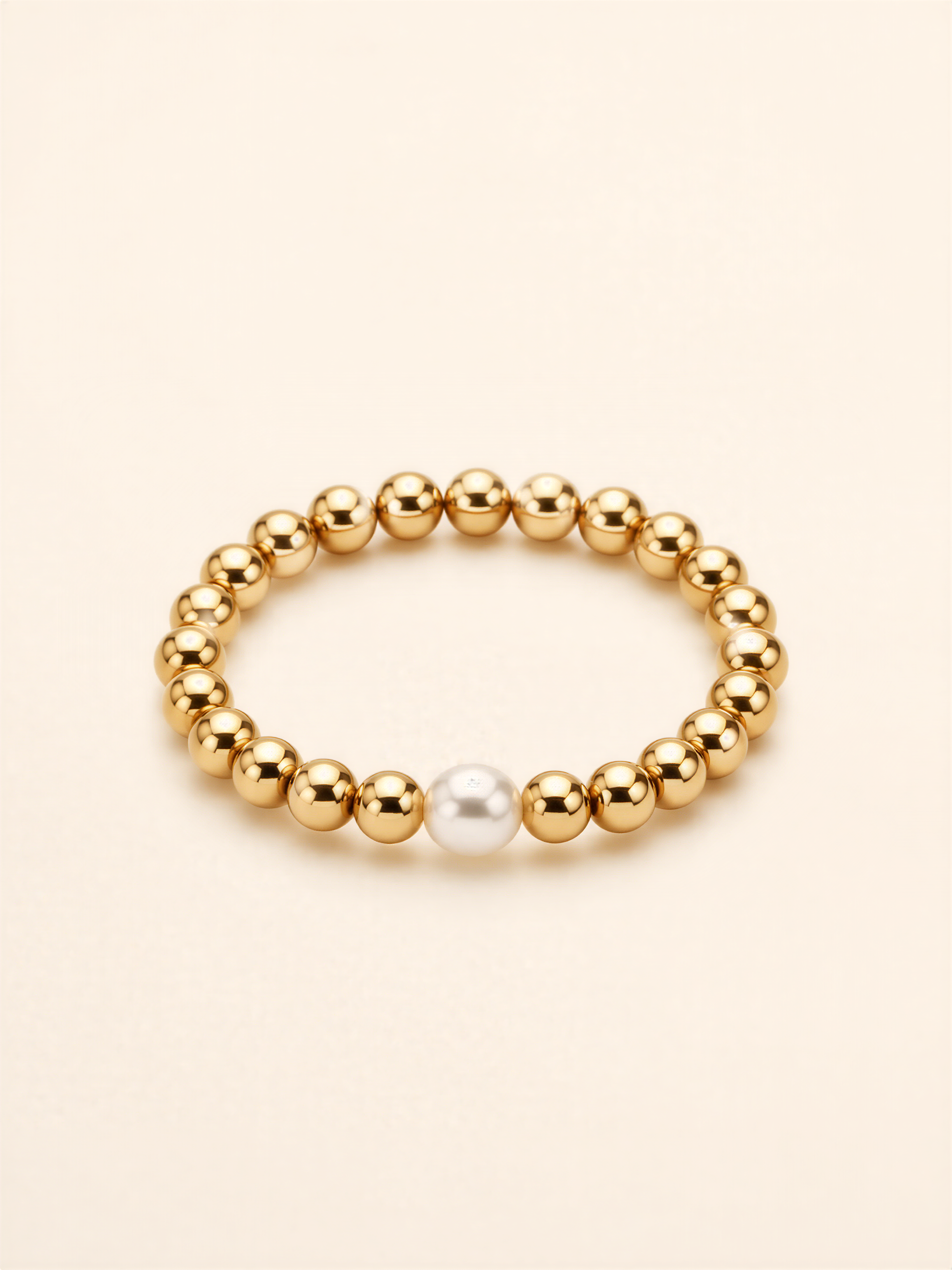 A gold-colored bracelet with a single white pearl bead in the center.