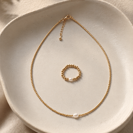 A delicate gold necklace with a round pendant and a small round ring are displayed on a white plate.