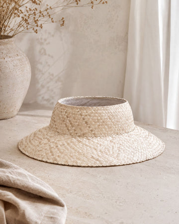 a straw hat with a woven pattern, placed on a light-colored surface.