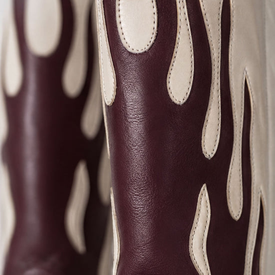 A close-up view of a pair of burgundy leather cowboy boots with flame-like designs on the sides.