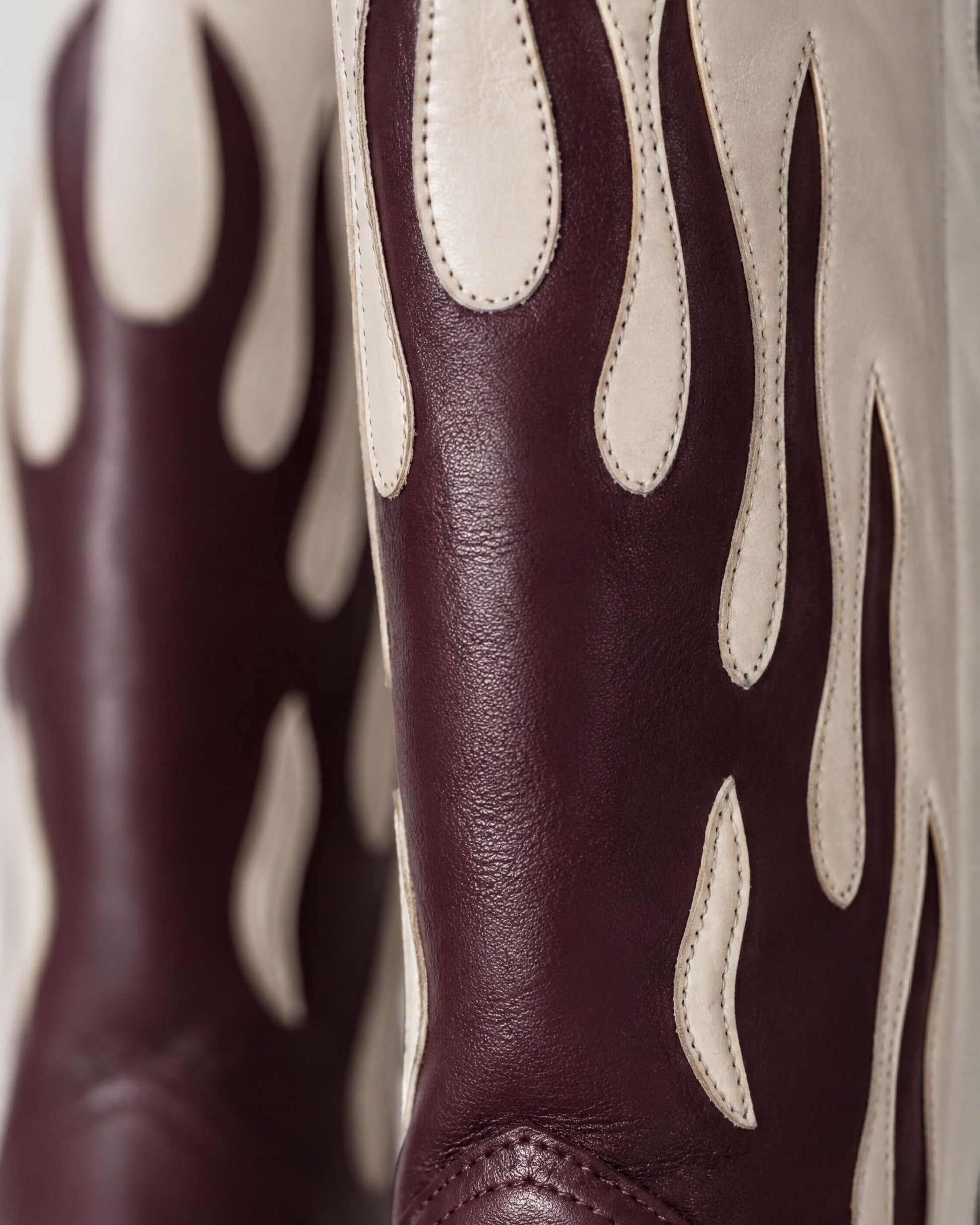 A close-up view of a pair of burgundy leather cowboy boots with flame-like designs on the sides.