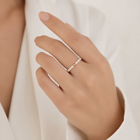 A close-up of a person's hand wearing a ring with pearls.