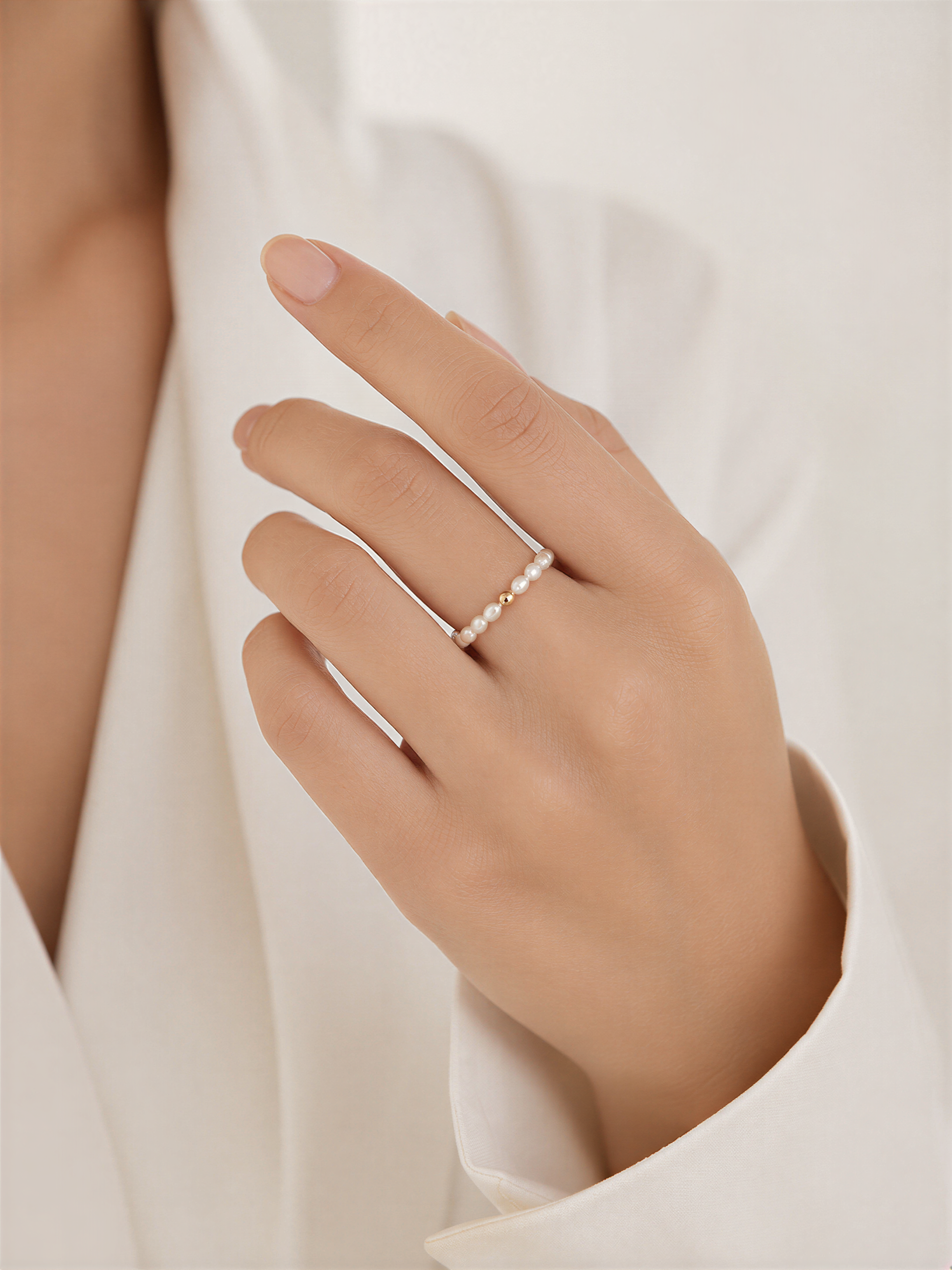 A close-up of a person's hand wearing a ring with pearls.