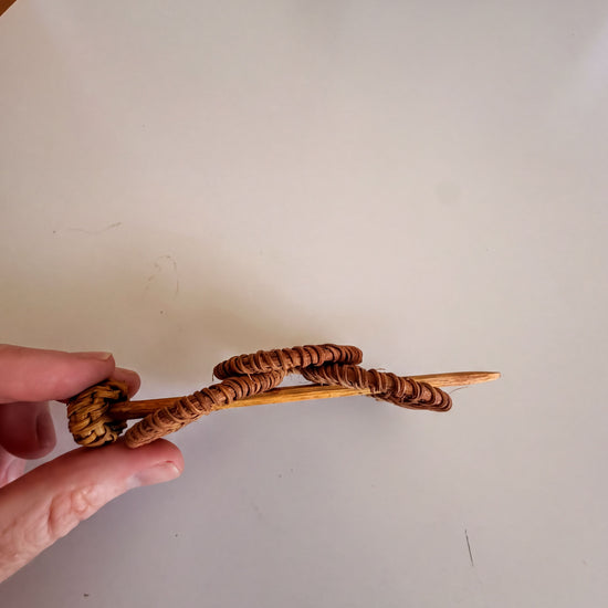A hand is holding a wooden object with a curved shape, which appears to be a piece of art or craftsmanship.