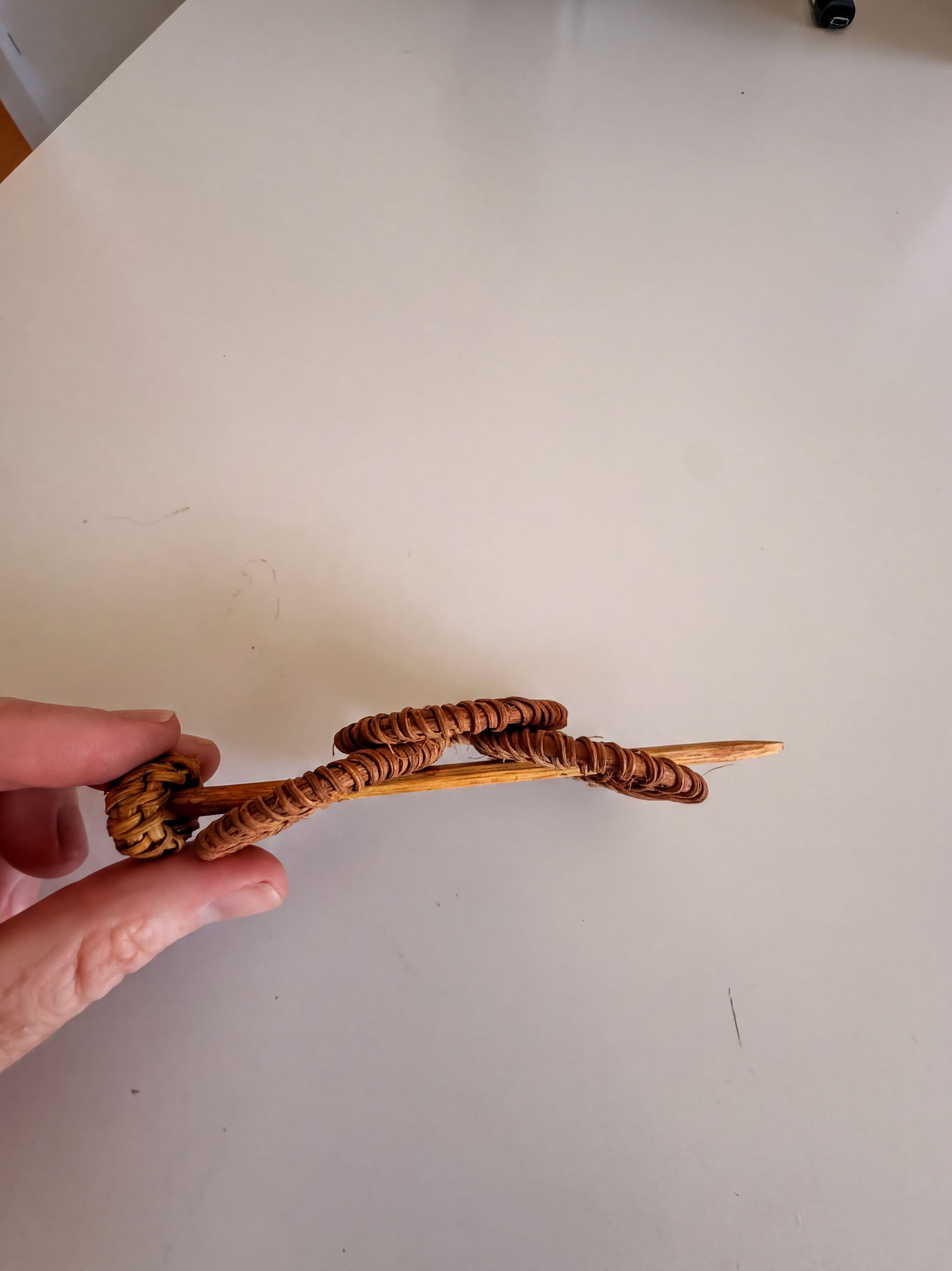 A hand is holding a wooden object with a curved shape, which appears to be a piece of art or craftsmanship.