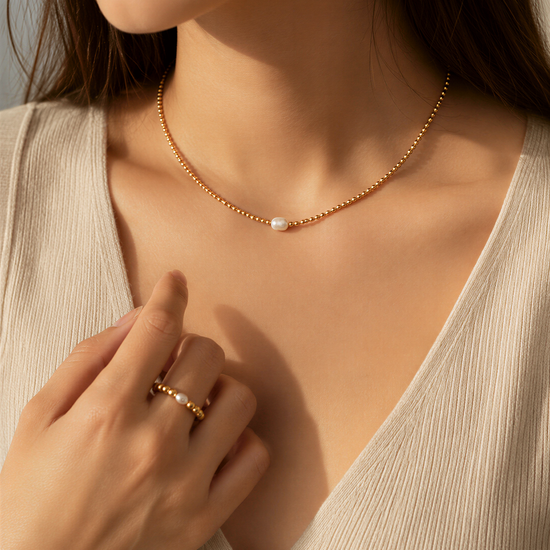 A close-up of a woman's hand wearing a gold necklace and ring, with her hair visible.