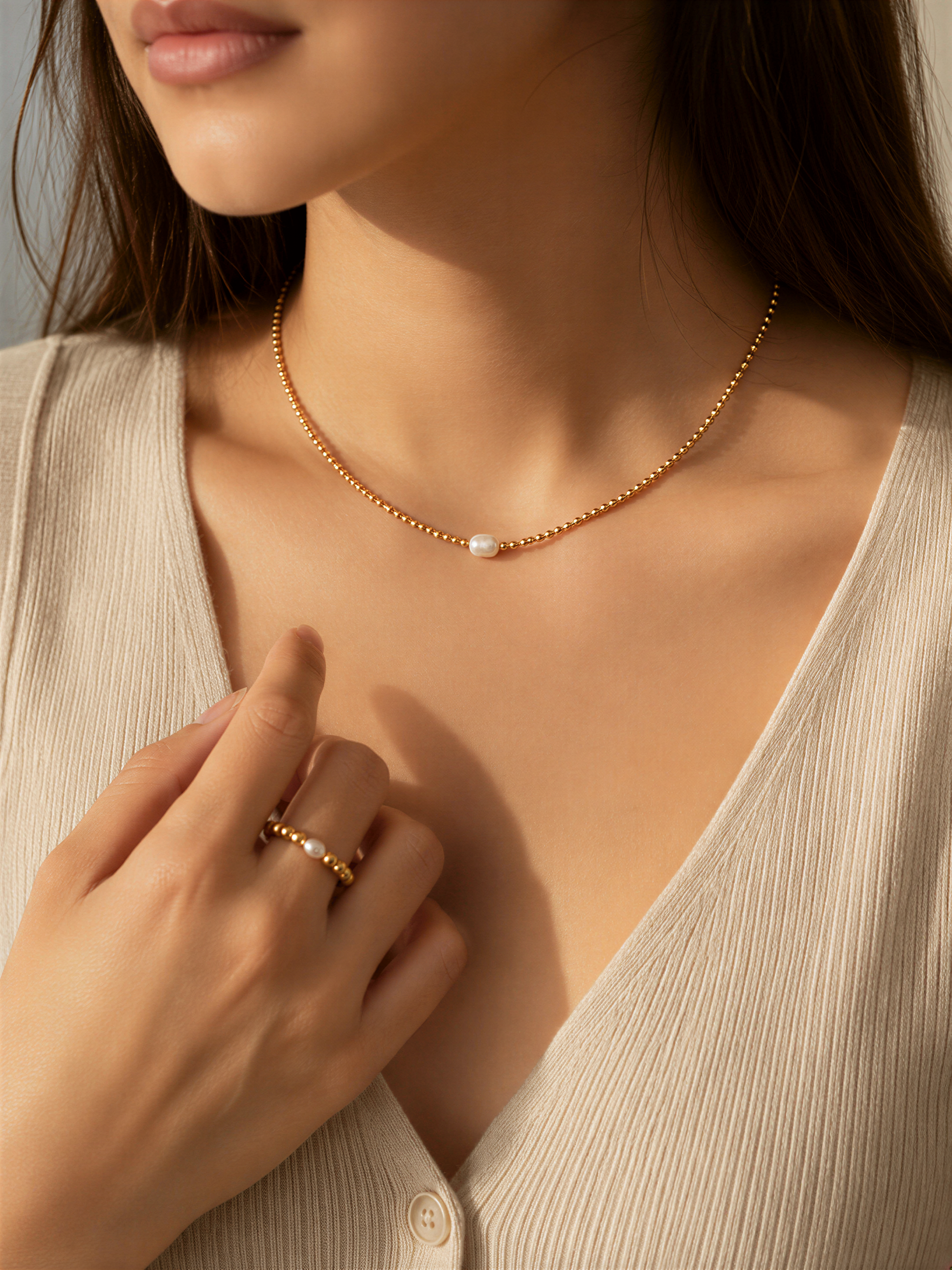 A close-up of a woman's hand wearing a gold necklace and ring, with her hair visible.