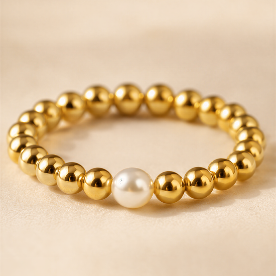 A gold-colored bracelet with a single white pearl bead in the center.