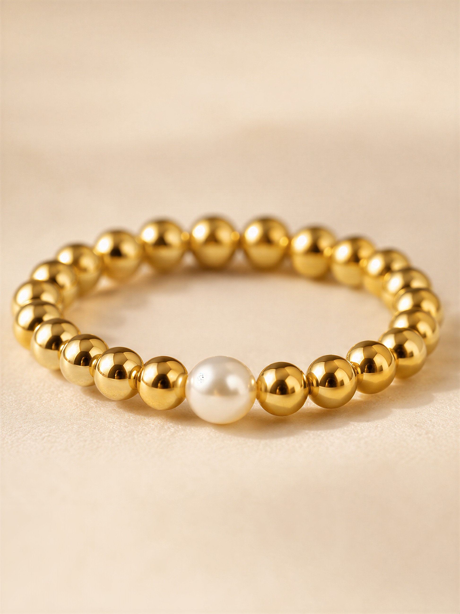 A gold-colored bracelet with a single white pearl bead in the center.