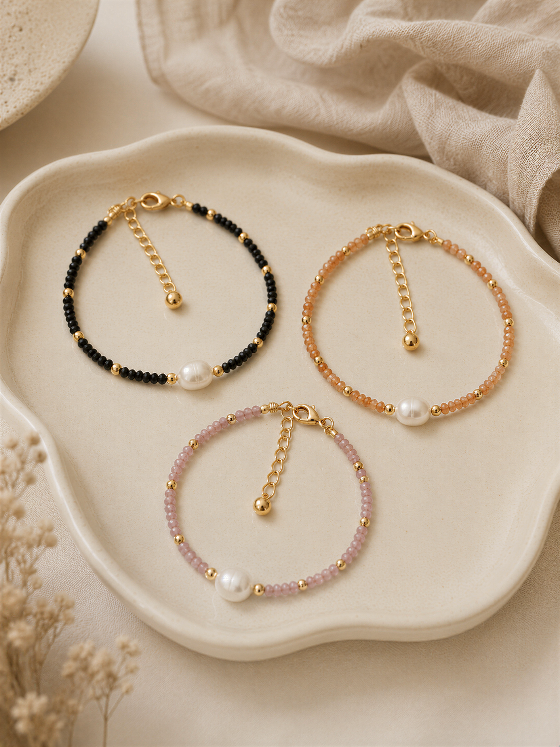 Three beaded bracelets with pearls are displayed on a white plate, arranged in a row.