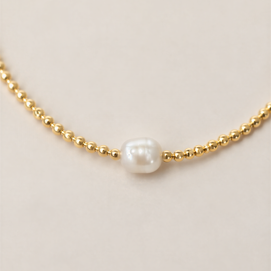 A delicate gold necklace with a single white pearl at the center.