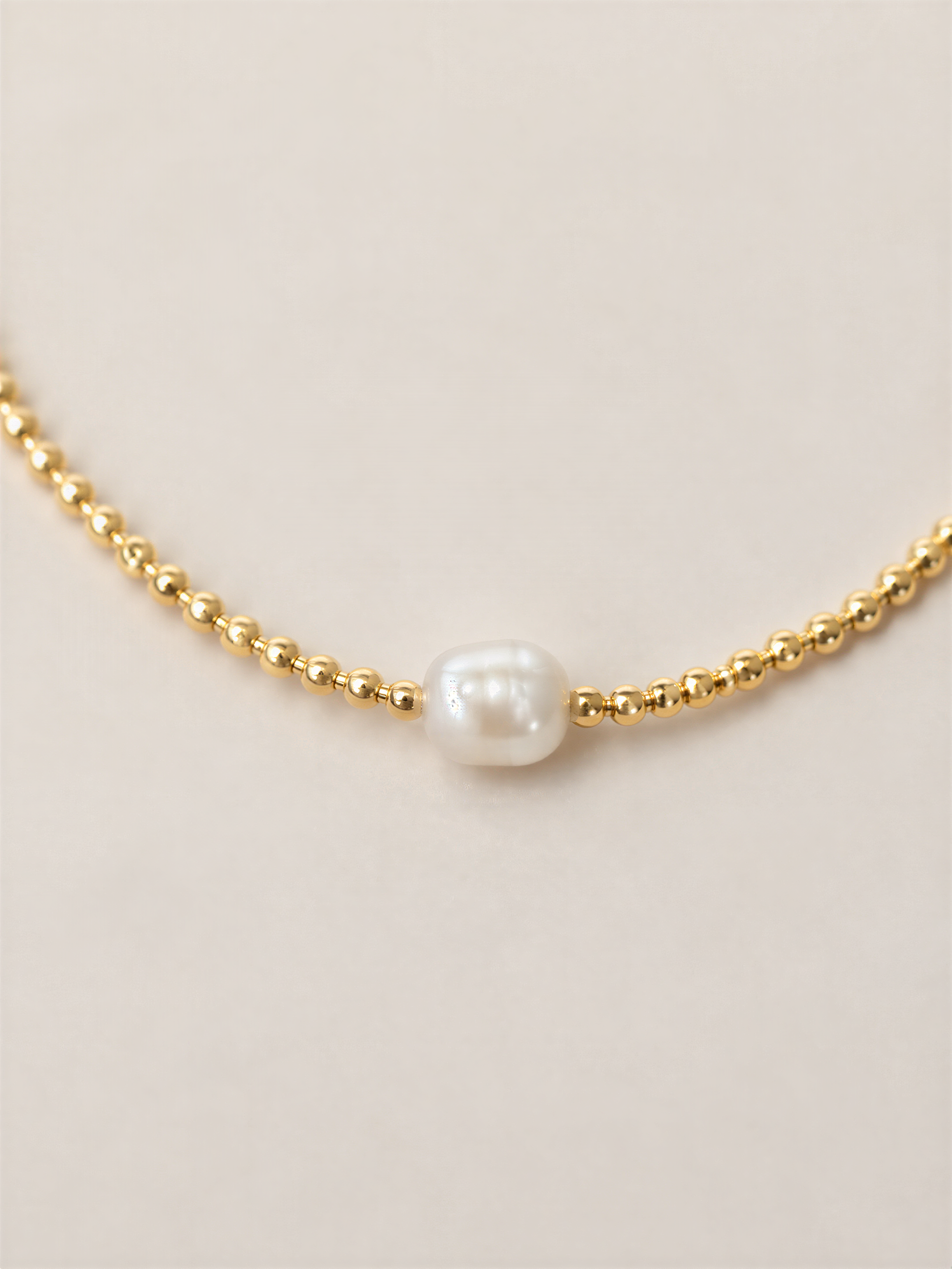 A delicate gold necklace with a single white pearl at the center.