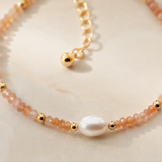 A delicate necklace with a pearl at the center, surrounded by a row of small, round beads in shades of orange and gold.