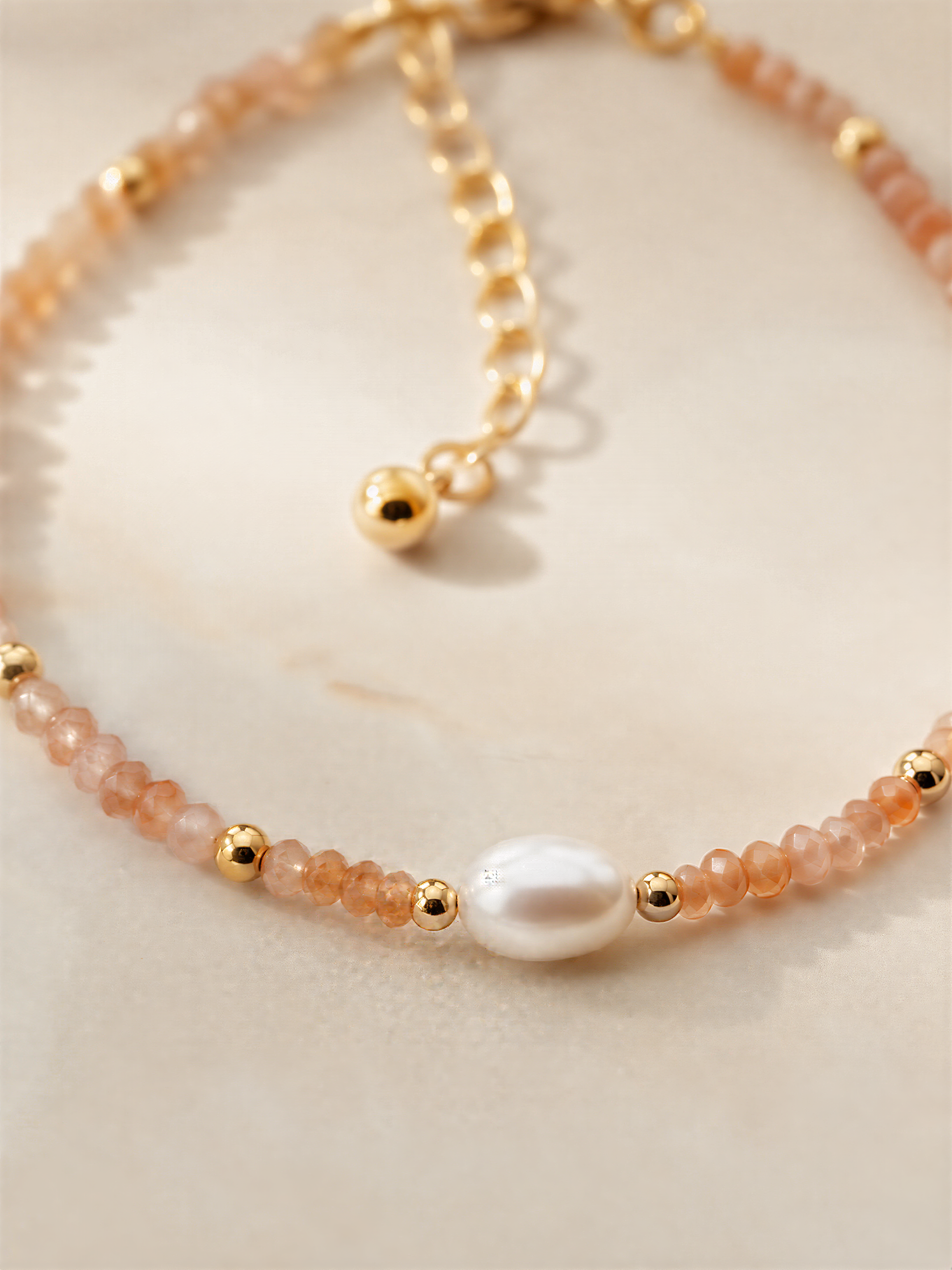 A delicate necklace with a pearl at the center, surrounded by a row of small, round beads in shades of orange and gold.