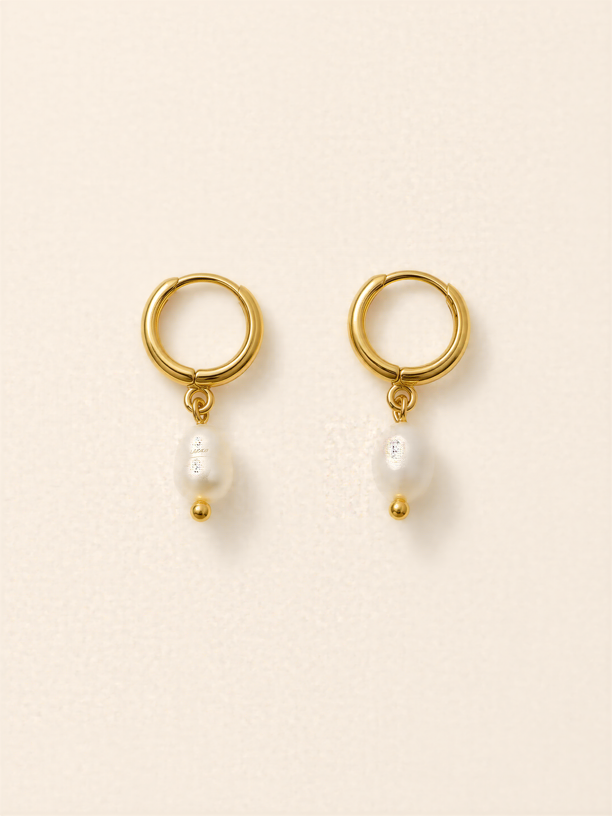 A pair of gold earrings with a pearl hanging from each earring.