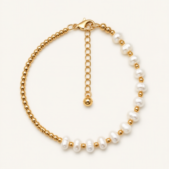 A gold-colored bracelet with a row of white pearls on one side and a clasp on the other side.