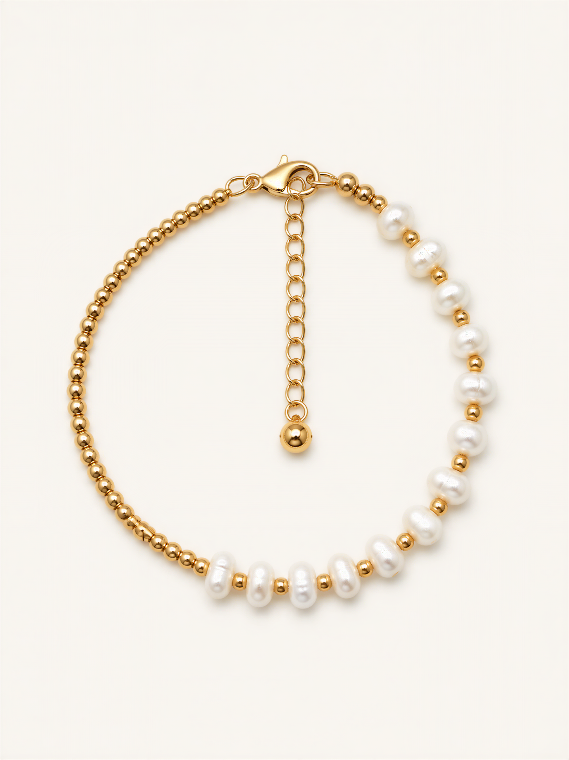 A gold-colored bracelet with a row of white pearls on one side and a clasp on the other side.