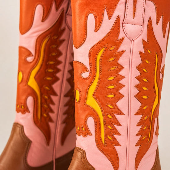 A close-up of a pair of colorful, patterned cowboy boots with a mix of pink and orange hues.