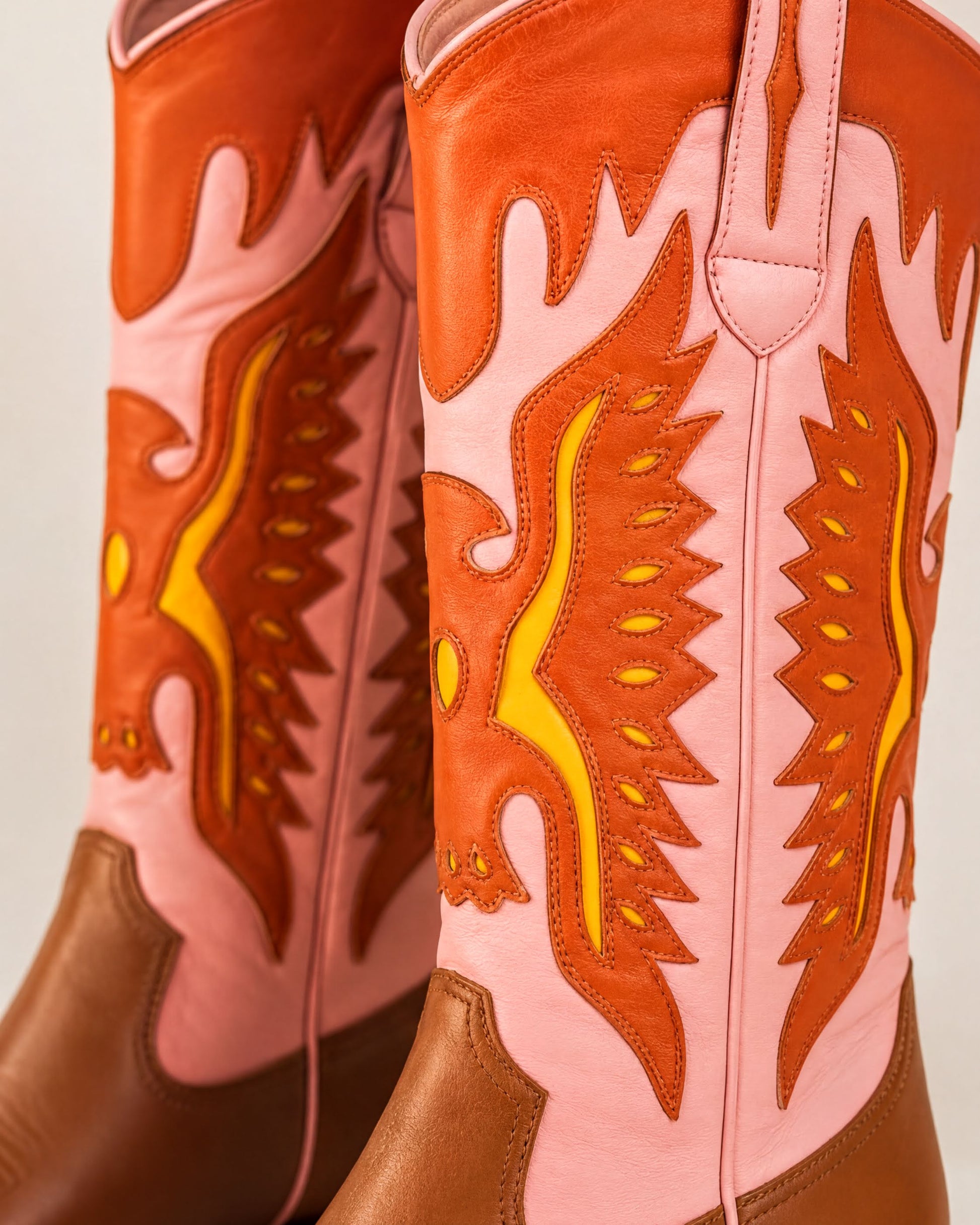 A close-up of a pair of colorful, patterned cowboy boots with a mix of pink and orange hues.