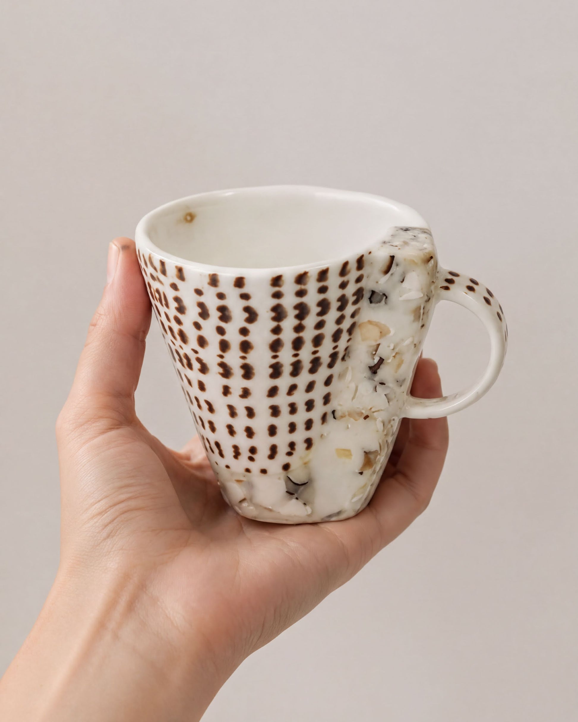 A hand holding a white mug with a brown patterned design.
