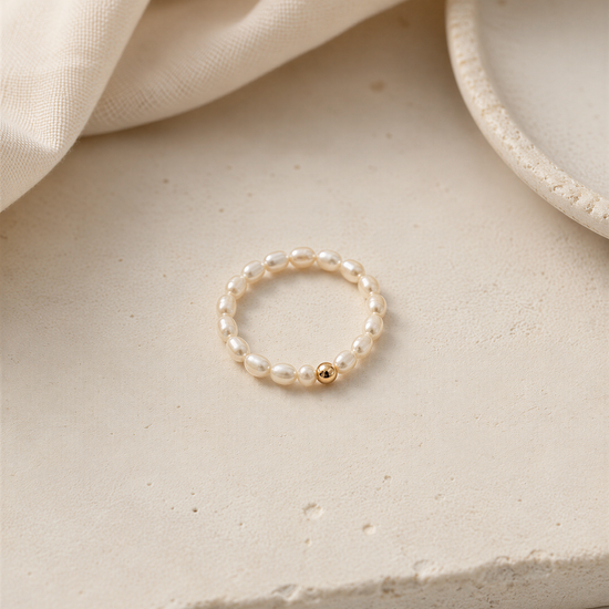 A delicate white pearl ring with a small gold accent is displayed on a light-colored surface.