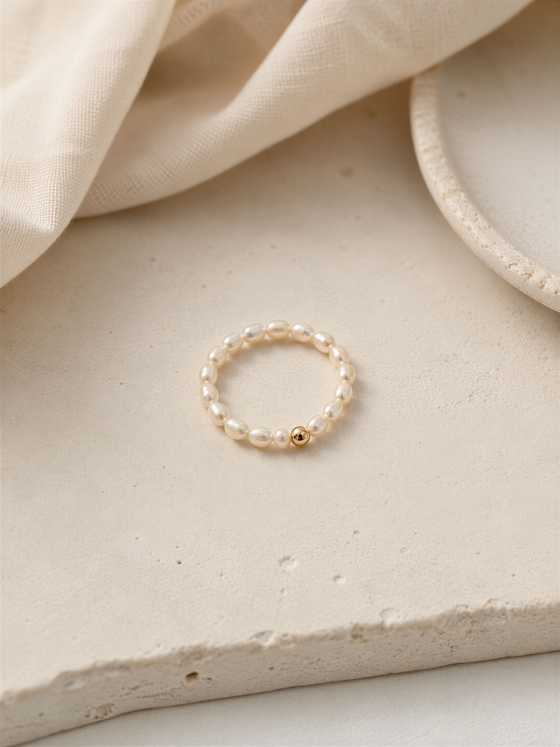 A delicate white pearl ring with a small gold accent is displayed on a light-colored surface.