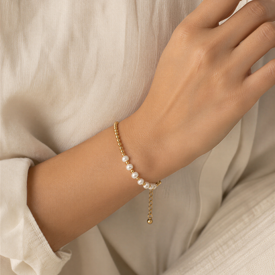 A close-up view of a person's hand wearing a delicate gold bracelet with white pearls.