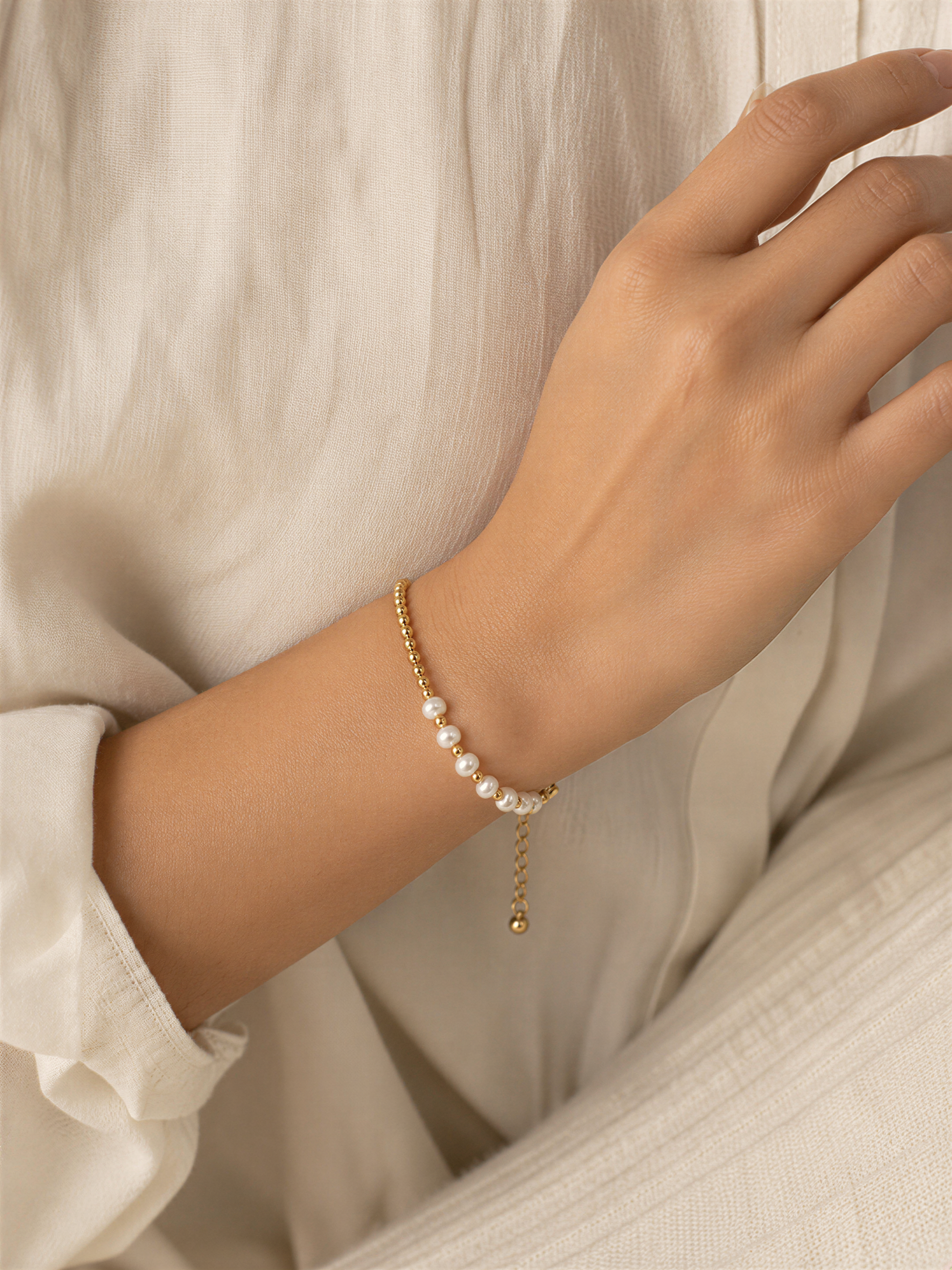 A close-up view of a person's hand wearing a delicate gold bracelet with white pearls.