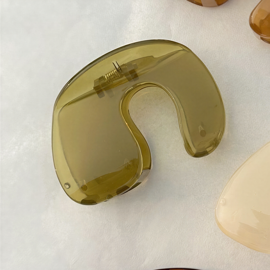 A close-up view of a yellow, curved object resembling a hair clip or bobby pin, placed on a white surface.