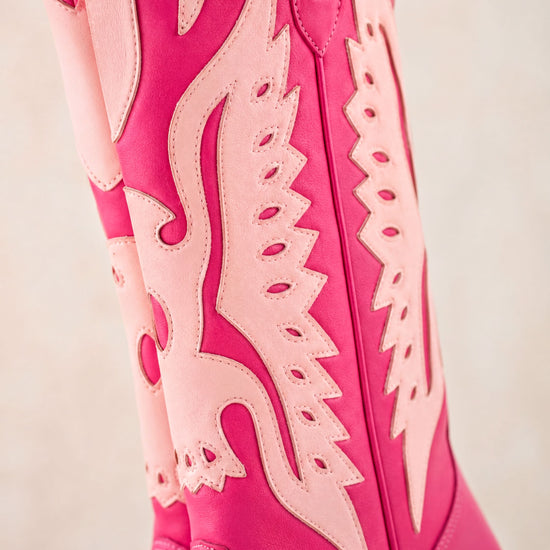 A close-up of a pair of pink cowboy boots with intricate cutout designs.