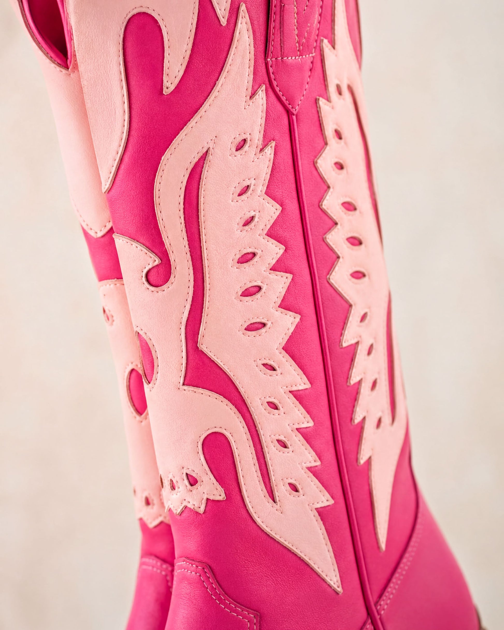 A close-up of a pair of pink cowboy boots with intricate cutout designs.