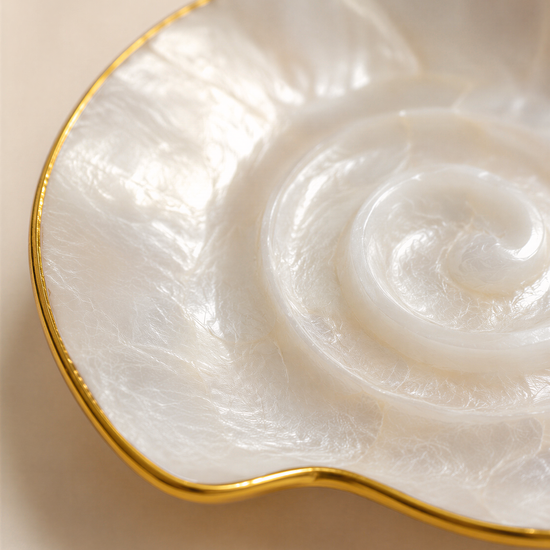 A close-up image of a white, spiral-shaped object with a gold rim, resting on a light-colored surface.