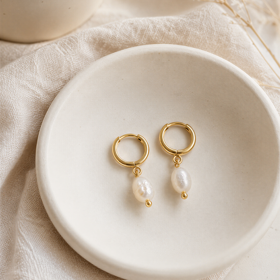 A pair of gold earrings with white pearls hanging from them, displayed on a white plate or bowl.