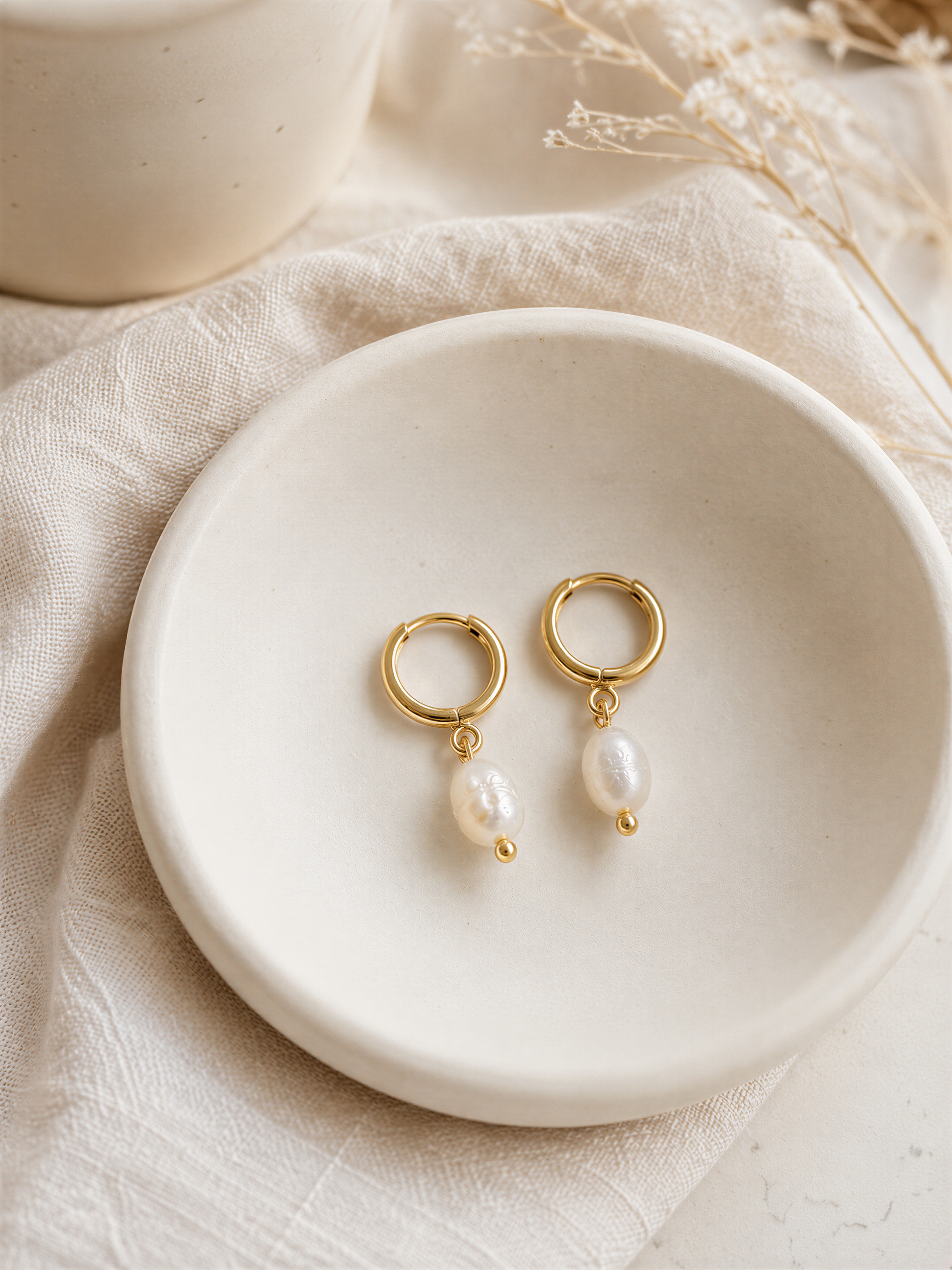 A pair of gold earrings with white pearls hanging from them, displayed on a white plate or bowl.