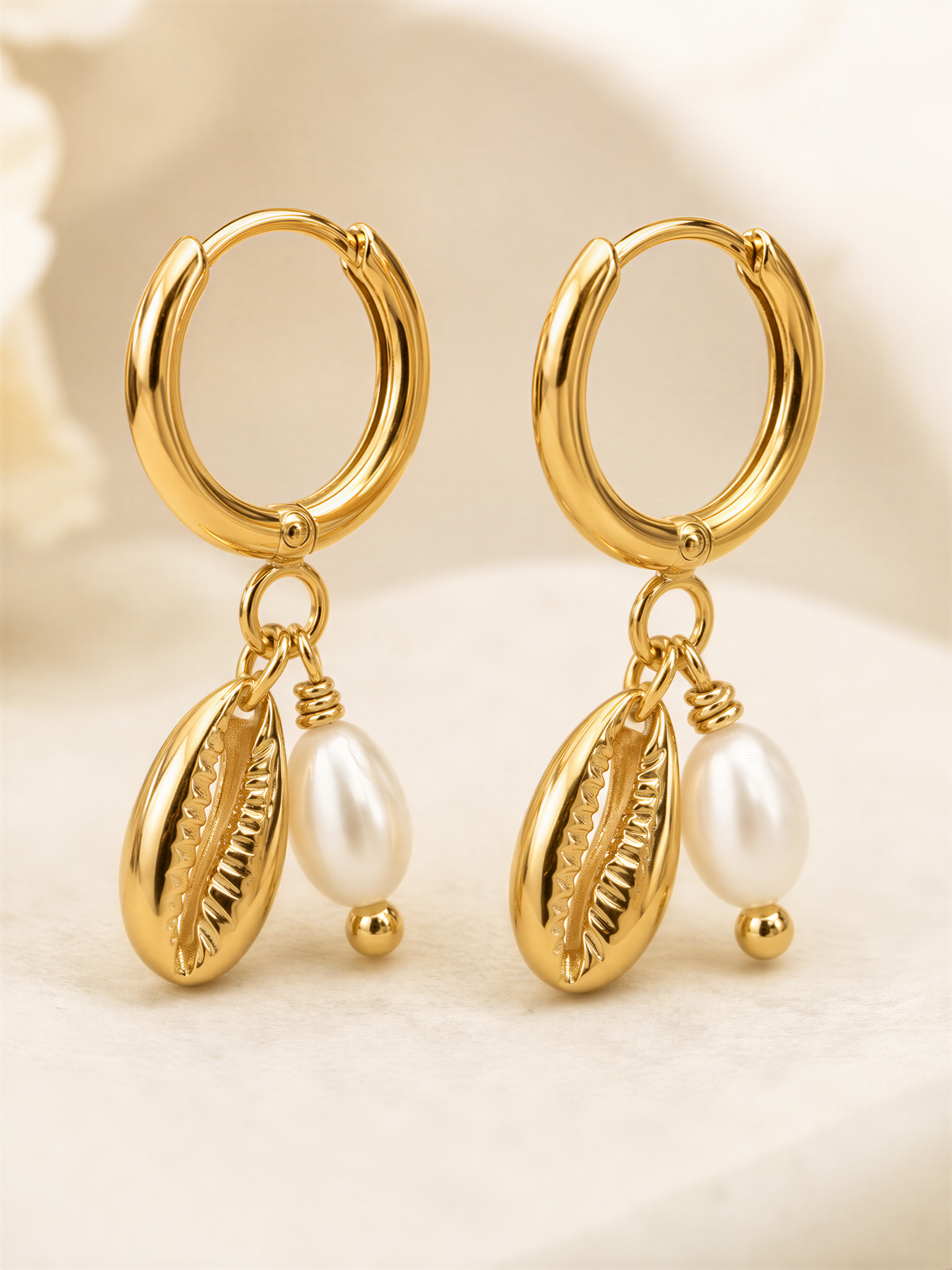 A pair of gold earrings with pearl accents and dangling charms.