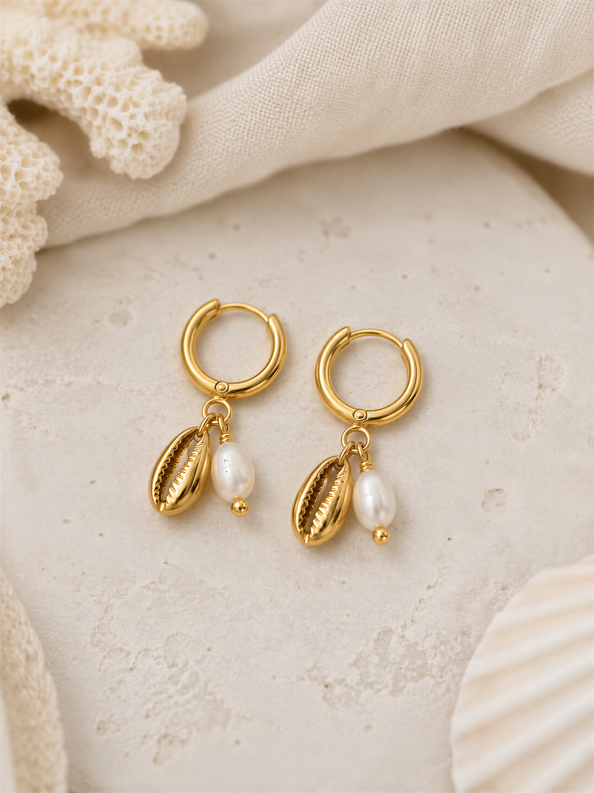 A pair of gold earrings with pearl accents and hoop earrings, resting on a white surface.