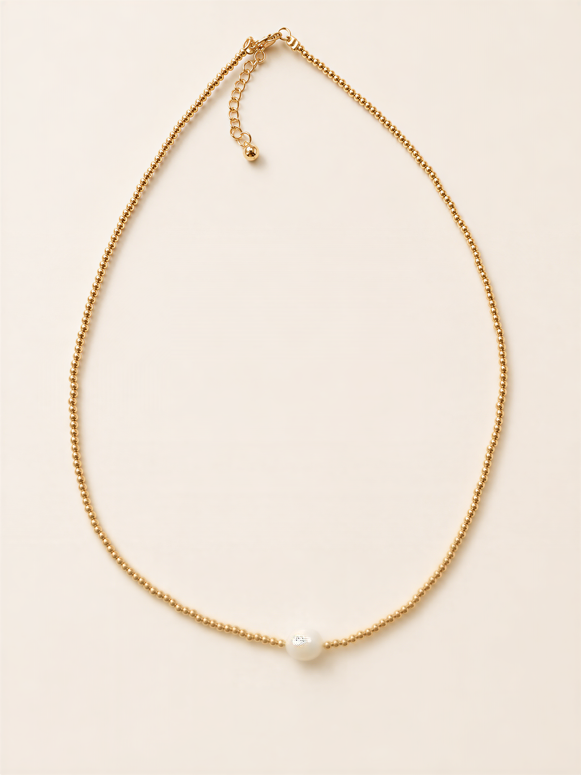 A delicate gold necklace with a single white pearl at the center.