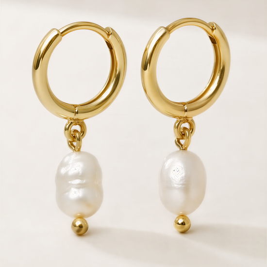 A pair of gold earrings with white pearls hanging from them.