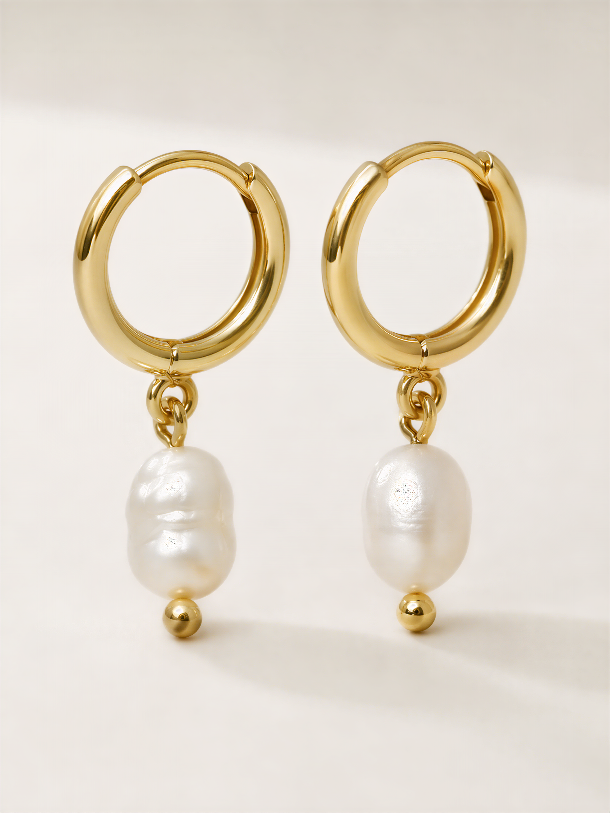 A pair of gold earrings with white pearls hanging from them.