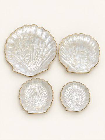 four white seashell-shaped plates with gold trim, arranged in a square formation against a white background.