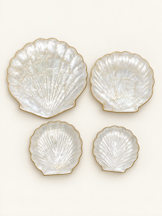 four white seashell-shaped plates with gold trim, arranged in a square formation against a white background.