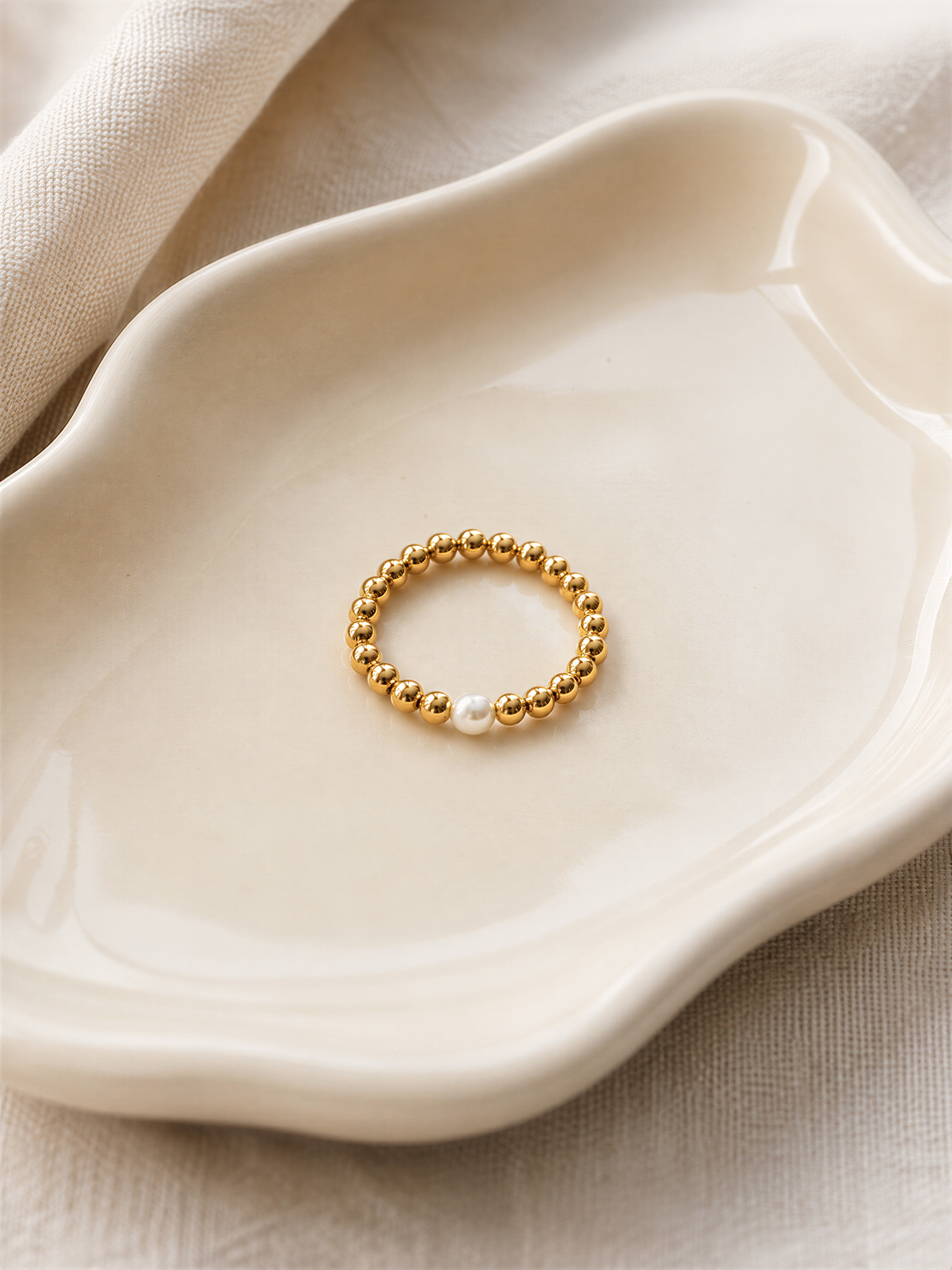 A gold-colored ring with a single pearl is displayed on a white ceramic plate.