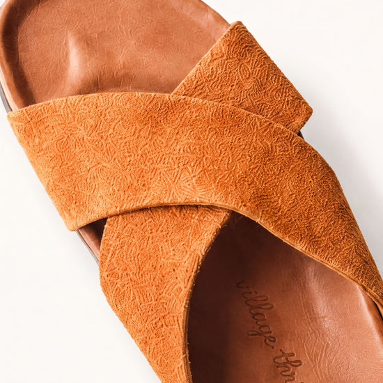 A close-up view of a brown suede sandal with a textured pattern.