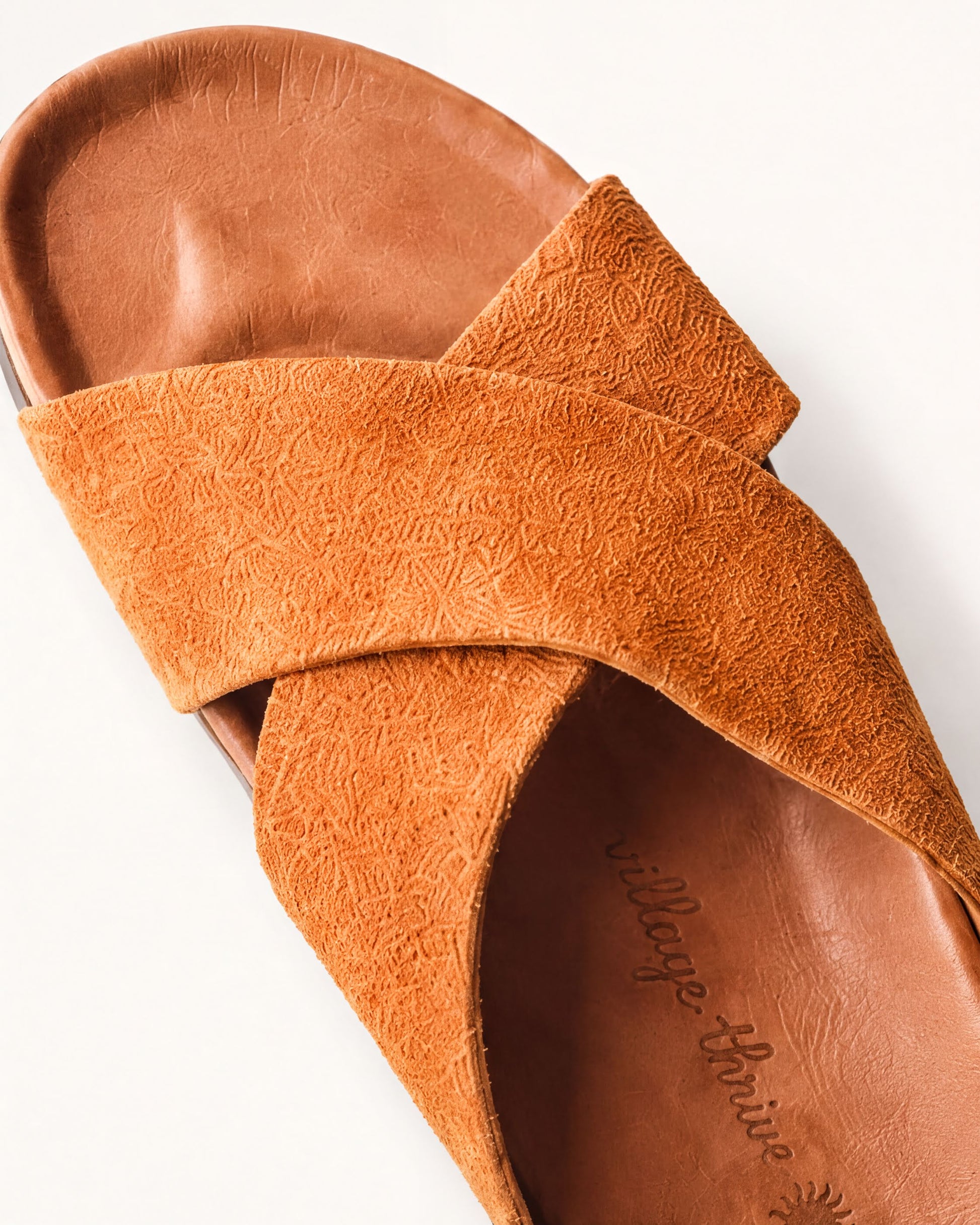 A close-up view of a brown suede sandal with a textured pattern.