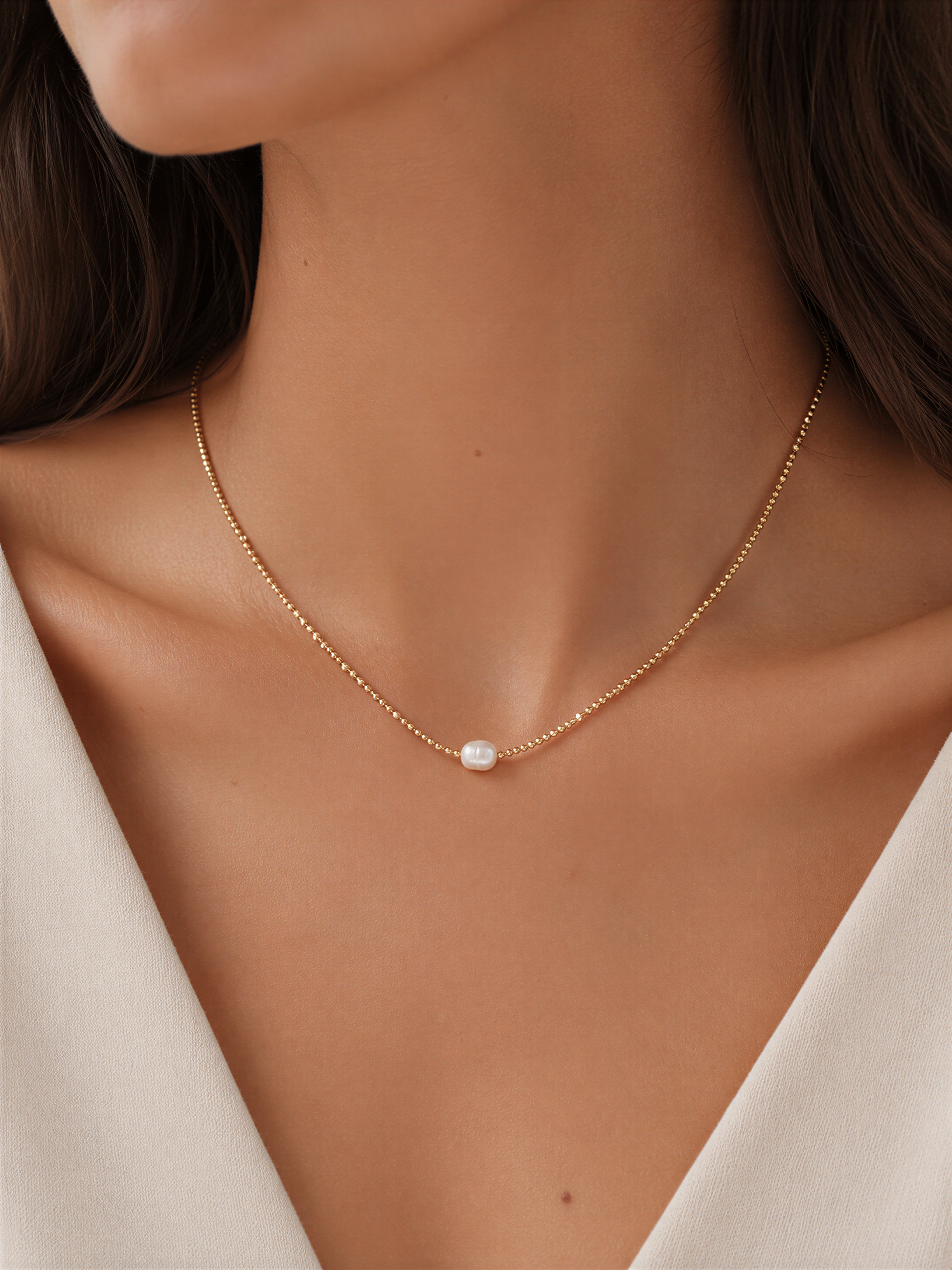 A close-up view of a woman's neck and chest area wearing a delicate gold necklace with a small white pearl pendant.